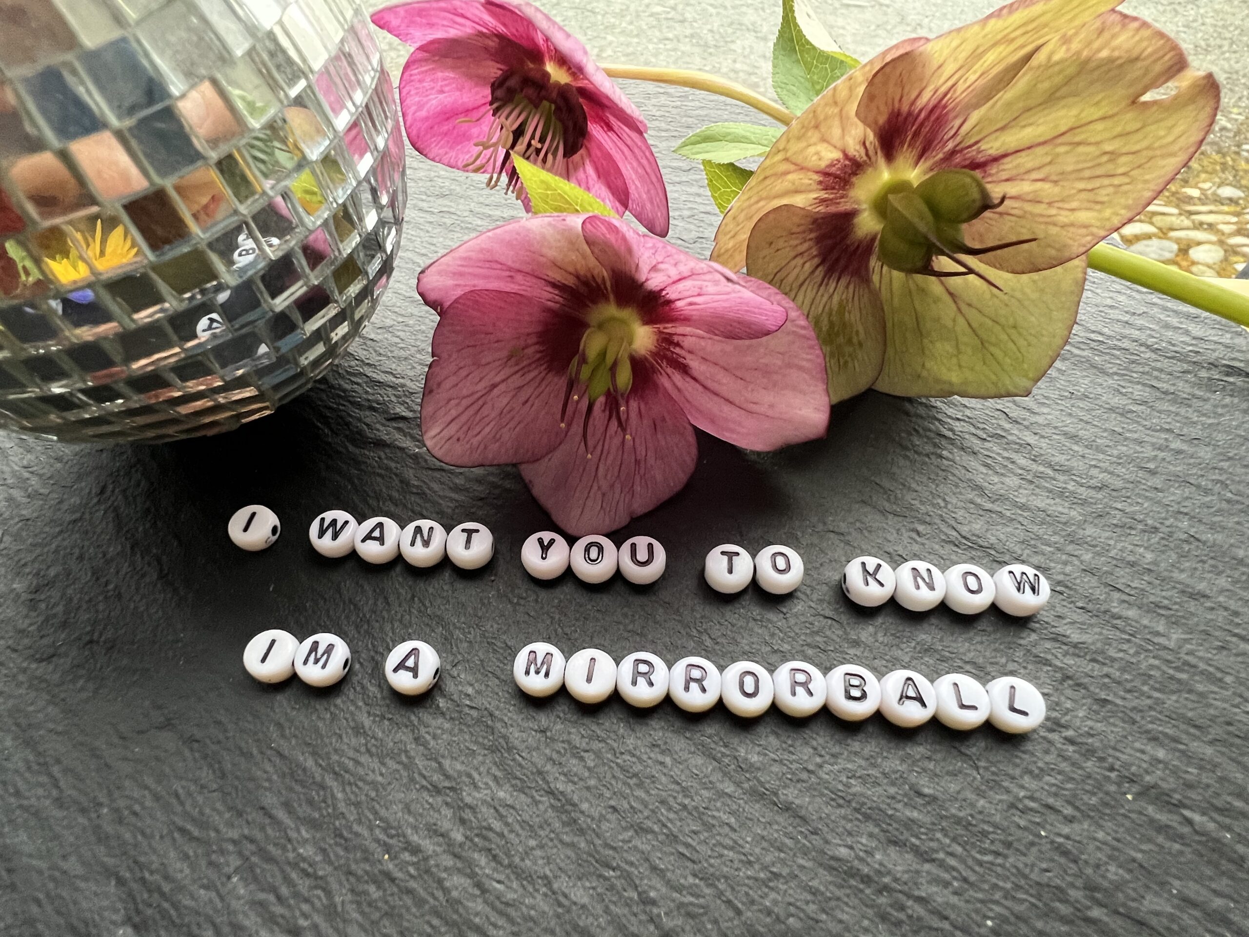 A slate with a mirrorball and flowers and letter beads that spell out I want you to know that I am a mirrorball